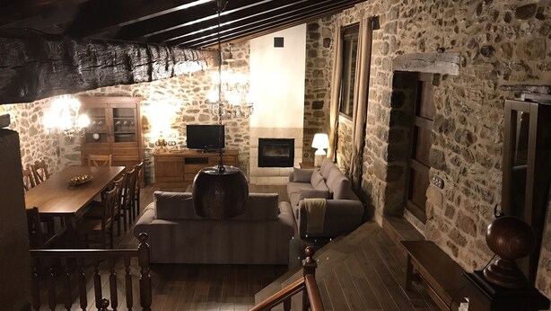 Una sala de estar acogedora con pared de piedra, muebles de madera, chimenea y televisor.