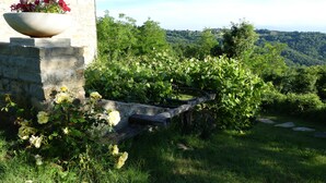 Un edificio de piedra con una jardinera con flores a la izquierda y un jardín exuberante con un muro de piedra y un puente de madera.