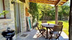 Un patio al aire libre con suelo de piedra, una mesa y sillas de madera, una parrilla y un muro de piedra.