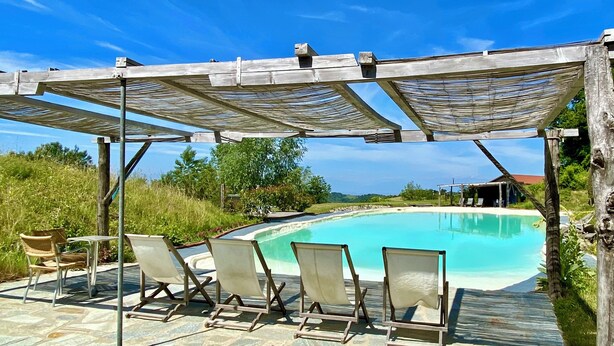 Un área de piscina con una pérgola de madera, sillas de descanso y un patio de piedra.