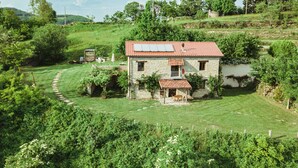 Una casa de piedra con techo de tejas rojas, rodeada de abundante vegetación y un cielo despejado.