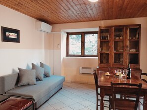 A room with a sofa, dining table, wooden cabinet, and a window with a view.
