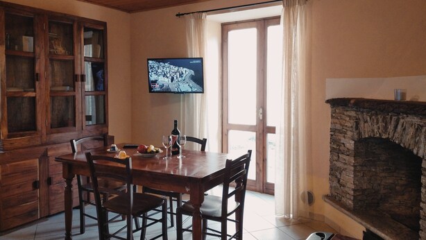 Un coin repas avec une table et des chaises en bois, un téléviseur fixé au mur et une cheminée en pierre.