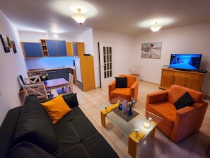 A living room with a sofa, two armchairs, a coffee table, a TV, and a kitchen area with cabinets and a refrigerator. - 2 Room B 2 - Wohnpark Binz (with indoor pool) (Binz)