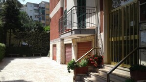 A building with a staircase leading to a balcony, a gated entrance, and a paved courtyard.