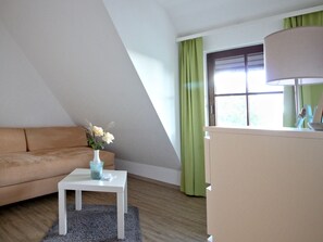 A modern living room with a sofa, a small table with a vase of flowers, a lamp, and a window with curtains.