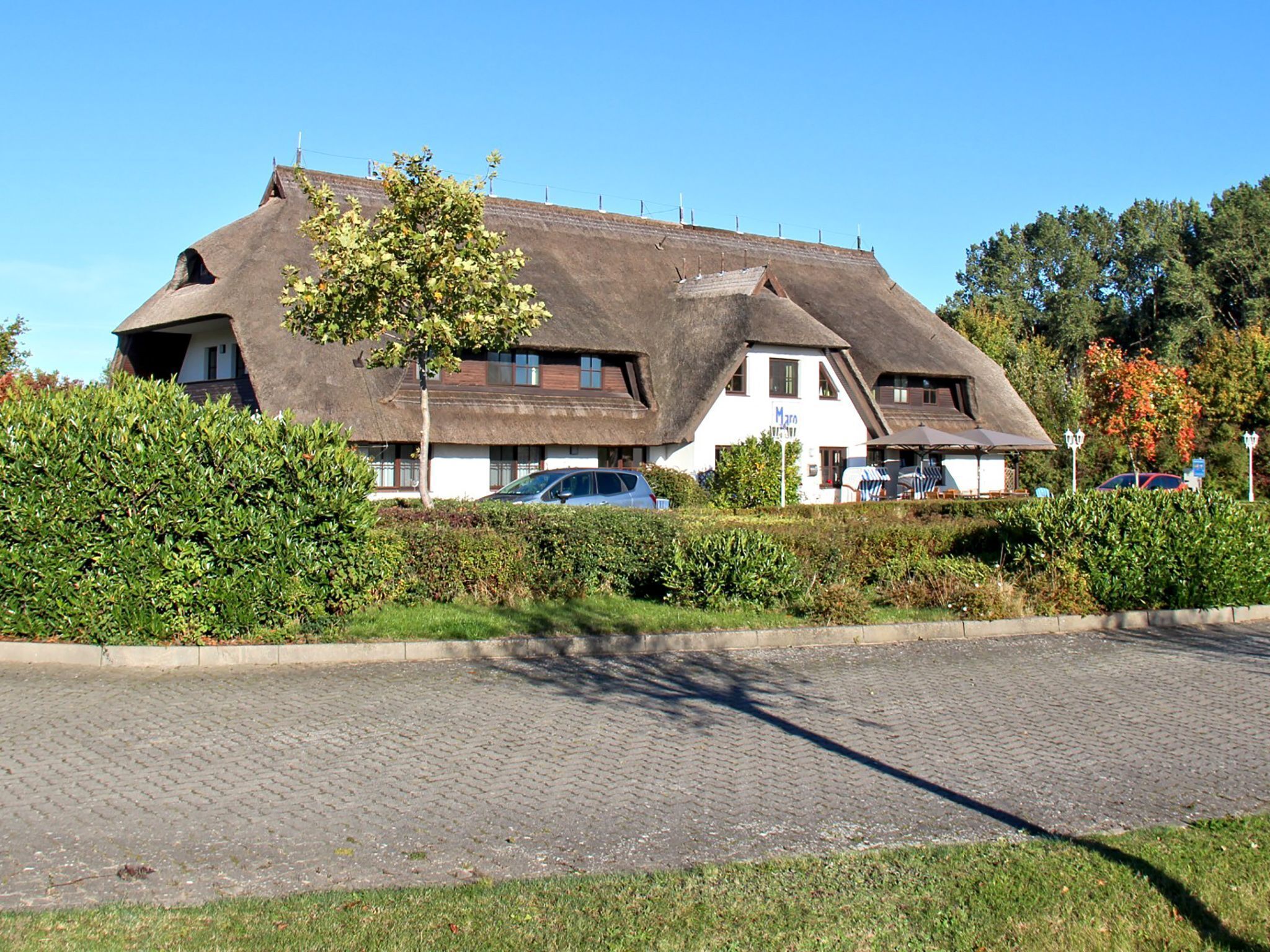 Une maison traditionnelle à toit de chaume, avec une allée pavée et une haie bien entretenue.