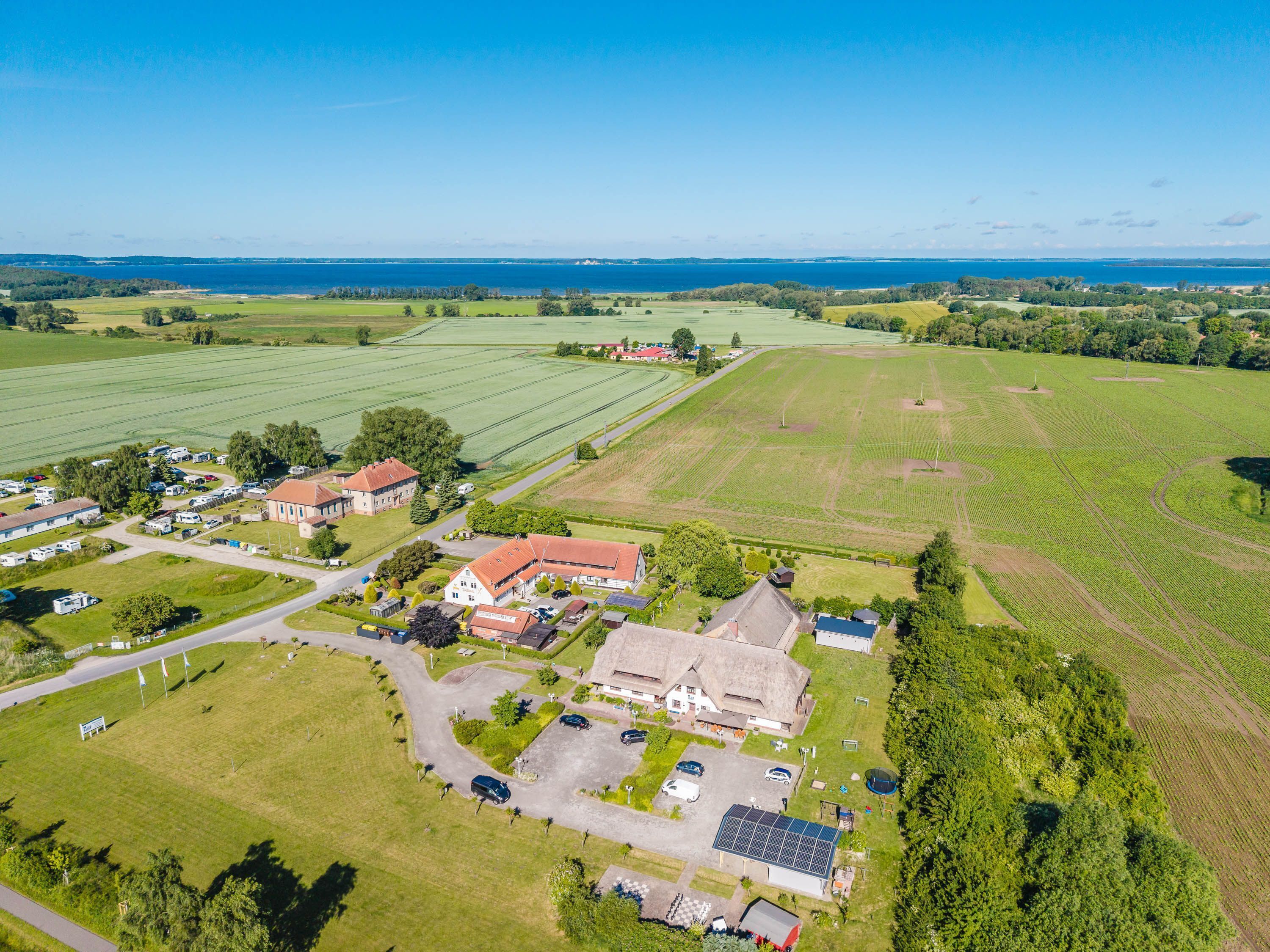 Eine Vogelperspektive auf eine ländliche Gegend mit einem großen Feld, einem Gebäude mit rotem Dach und mehreren parkenden Fahrzeugen.