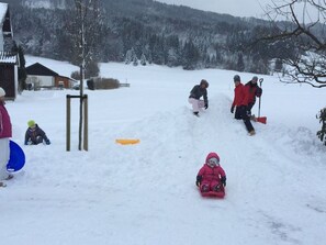 A snowy outdoor scene with a sled, a person in a red jacket, and a child in a pink snowsuit. - Family Room 6 - Pension ANNA, Apartments & Comfort Rooms *** (Keuschen)
