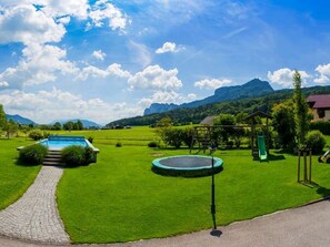 A well-maintained lawn with a swimming pool, a trampoline, and a small house with a red roof.