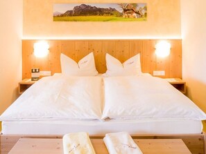 A double bed with white linens, two bedside tables with lamps, and a framed picture above the bed.