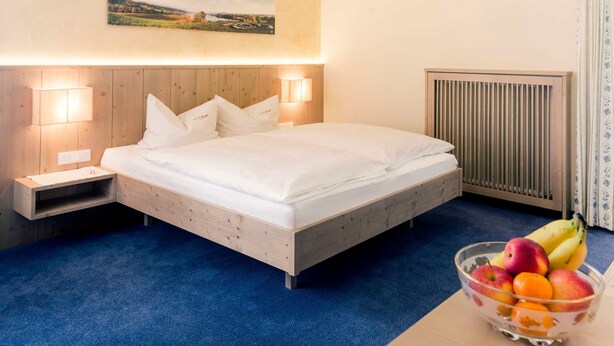 A bedroom with a wooden bed, bedside lamps, a nightstand, a radiator, and a bowl of fruit on a table.