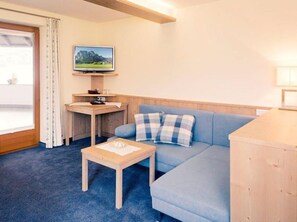 A room with a blue sofa, a wooden coffee table, a TV on a stand, and a window with curtains.
