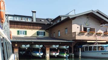 A boat docked at a marina with a building featuring a balcony with flower boxes.