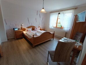 A bedroom with a wooden bed, bedside tables, a desk with a chair, a window with curtains, and a radiator. - 8 - "Up'n Hoff", Germany (Middelhagen)