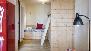 Quarto compacto com cama, um armário vermelho, escada e abajur.