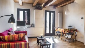 Uma sala de estar acolhedora, com um sofá vermelho, televisão e uma área de jantar com mesa e cadeiras.