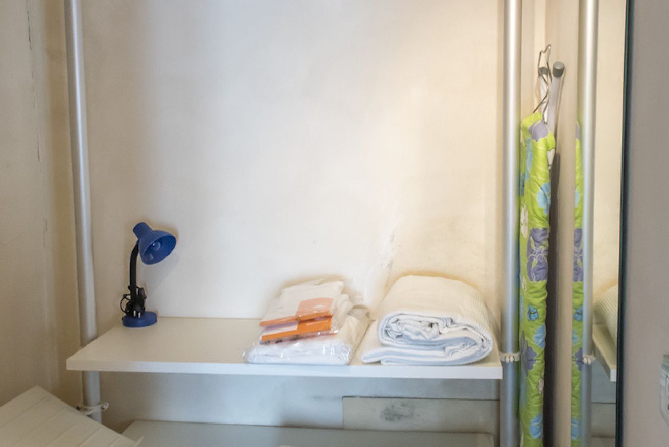 Een badkamer met een wit wastafelmeubel, een blauwe lamp, een plank met opgevouwen handdoeken en een douchegordijn.