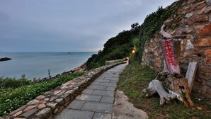 Un sentier de pierres mène à une zone côtière d’où l’on peut admirer la mer, et un mur de pierres est orné de caractères chinois.