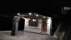 Un edificio pequeño y bien iluminado con fachada de ladrillo y puerta de madera, con lámparas colgantes y techo inclinado.