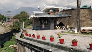 Un edificio pequeño con techo inclinado, fachada de piedra y una serie de macetas rojas a lo largo de un muro de piedra.