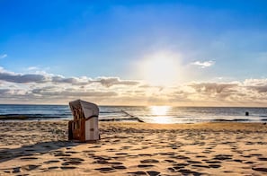 Une chaise de plage et une structure en bois sur une plage de sable, avec l’océan et un coucher de soleil en arrière-plan.