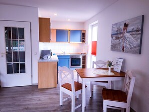 Una cocina moderna con armarios azules, una encimera de madera y una zona de comedor con sillas blancas y una mesa.