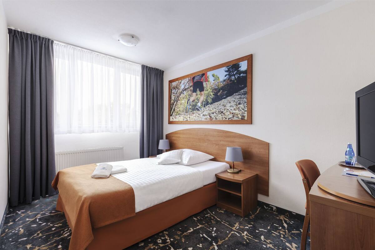 Ein Hotelzimmer mit Bett, Schreibtisch, Sessel, Fernseher und einem Bild an der Wand.