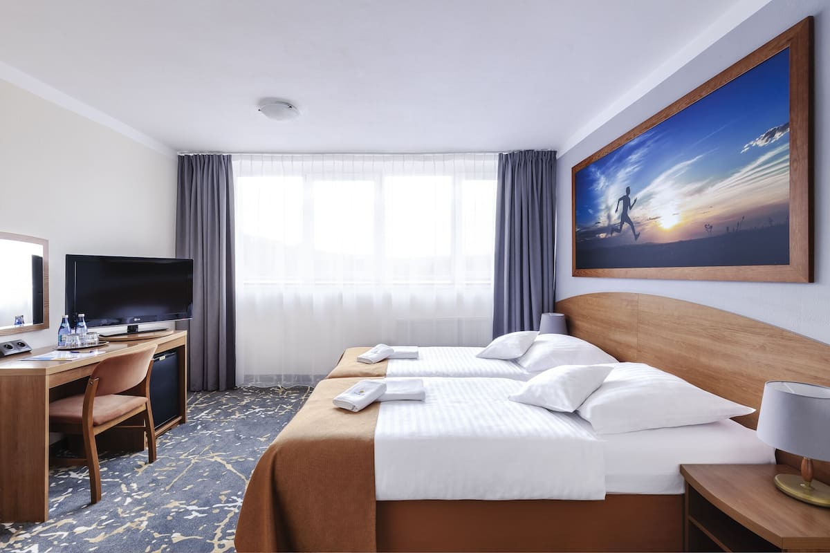 Ein Hotelzimmer mit zwei Betten, einem Schreibtisch, einem Fernseher, einem Computer und einem Fenster mit Vorhängen.