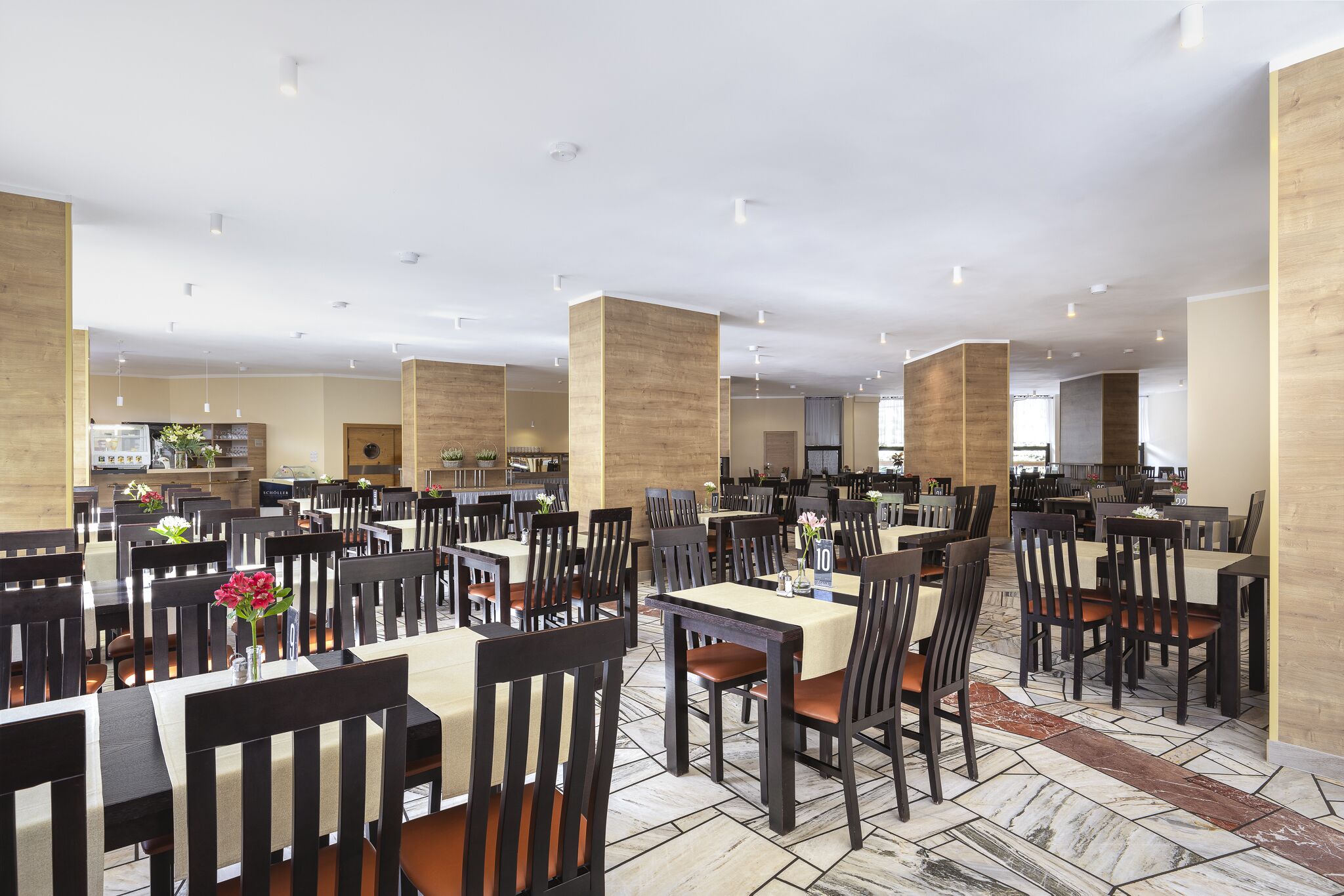 Un comedor amplio con varias mesas y sillas, techos altos y un diseño moderno y limpio.