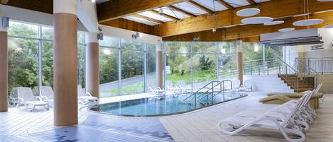 Un área de piscina interior con sillas de descanso, una piscina y ventanas amplias que ofrecen vistas al exterior.