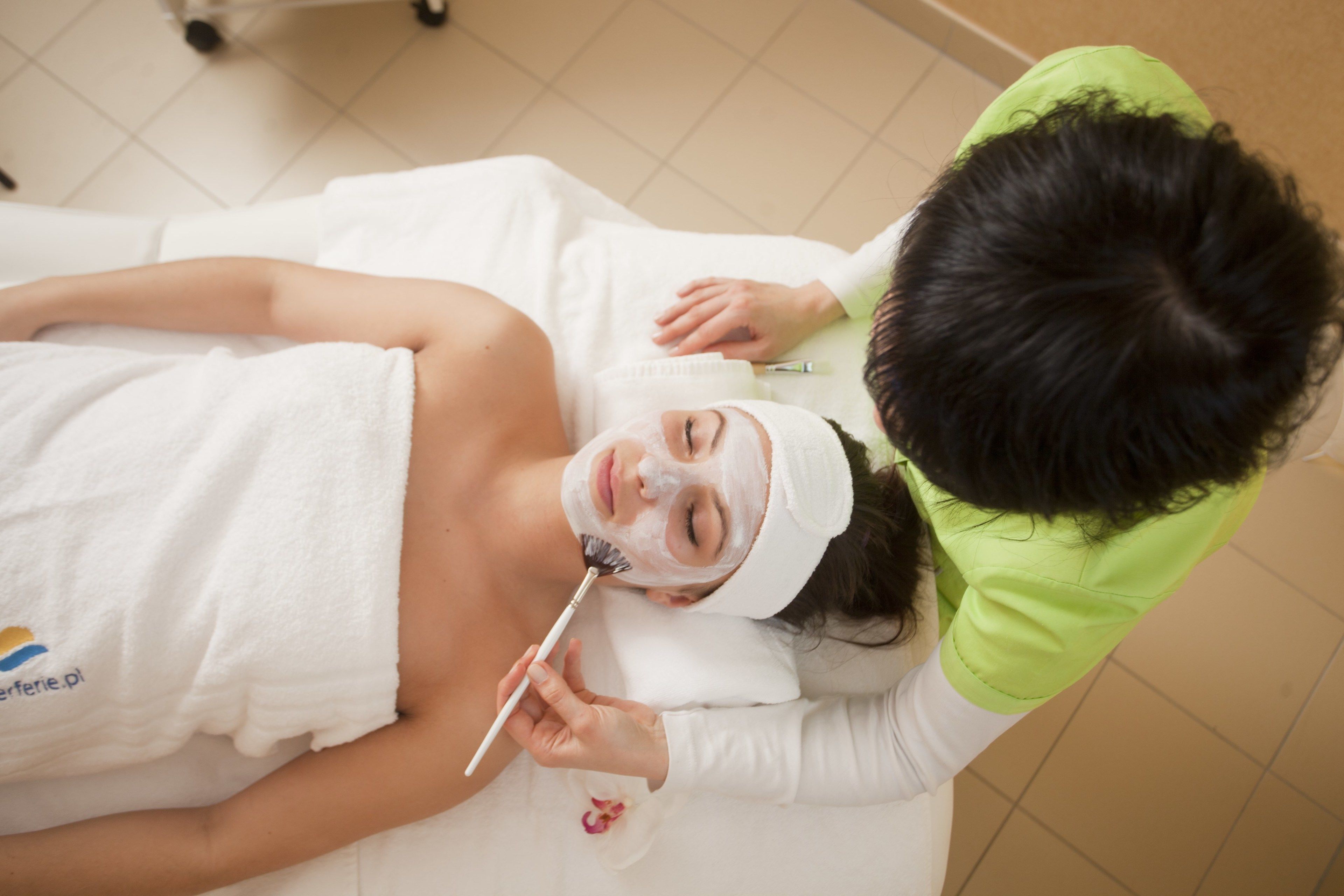 A person lying on a bed with a towel, receiving a facial treatment.