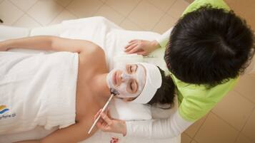 A person lying on a bed with a towel, receiving a facial treatment.