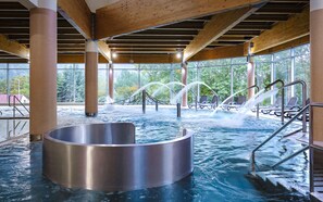 An indoor hot tub area with a circular hot tub, wooden beams, and a view of trees through large windows. - Interferie Aquapark Sport Hotel Malachit (Swieradow-Zdroj)