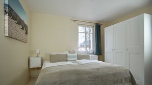 Une chambre à coucher comprenant un lit, une table de chevet, une fenêtre avec des rideaux et une armoire.
