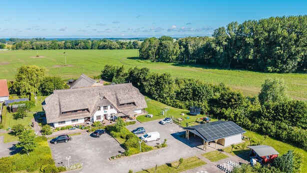 A large building with a thatched roof, surrounded by a parking area and greenery.