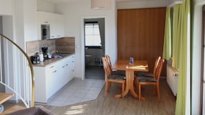 A modern kitchen with white cabinets, a microwave, and a coffee maker. There is a dining area with a wooden table and chairs.