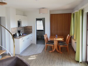 A modern kitchen with white cabinets, a microwave, and a coffee maker. There is a dining area with a wooden table and chairs.