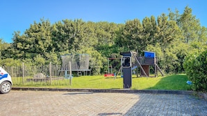 A paved area with a playground, a fence, and a vehicle.