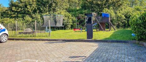 A paved area with a playground, a fence, and a vehicle.