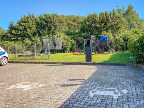 A paved area with a playground, a fence, and a vehicle.