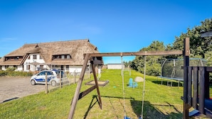 A house with a thatched roof, a swing set, and a trampoline in the yard.