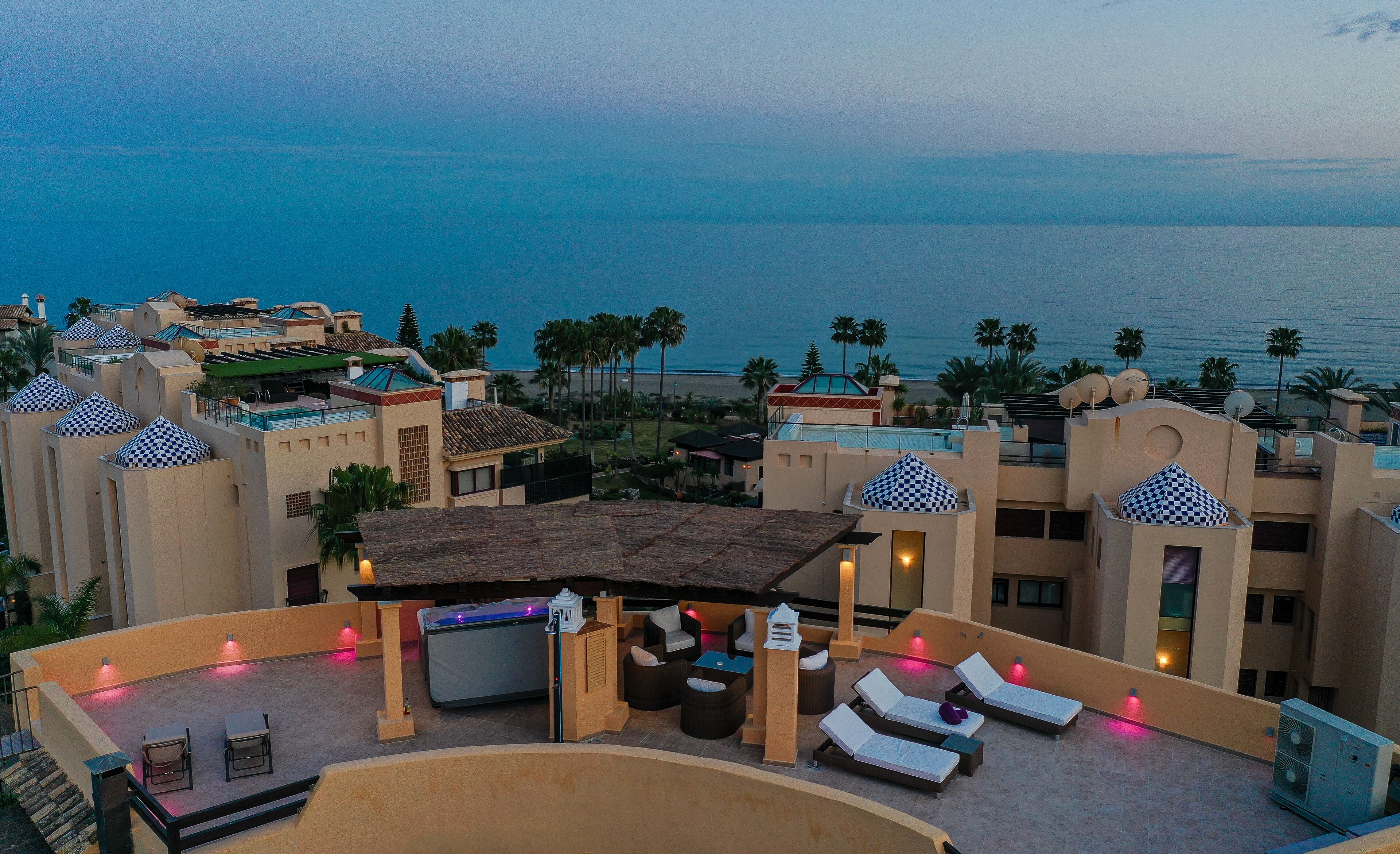 Un salon sur le toit, doté de chaises longues et d’un jacuzzi, offrant une vue sur une plage et l’océan.