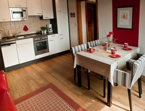 A modern kitchen with white cabinets, a microwave, and a coffee maker. There is a dining table with striped chairs and red tableware.
