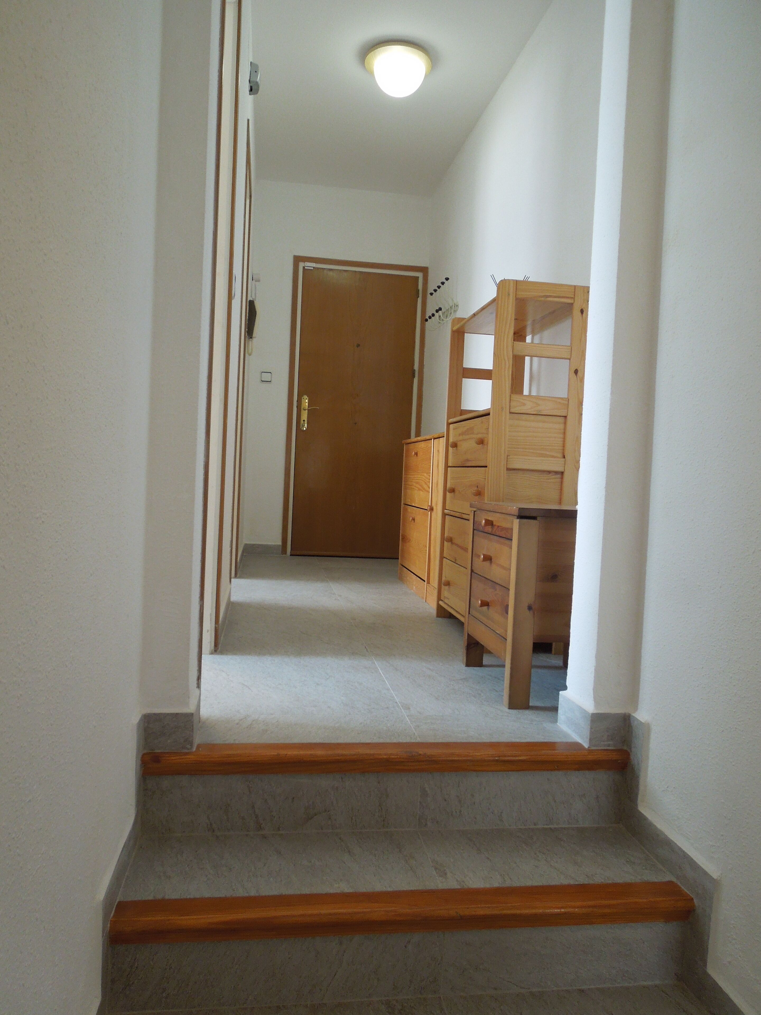 Een trap die leidt naar een deur, met een houten dressoir en een spiegel.