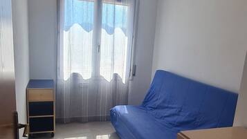 Un dormitorio con cama, cómoda, escritorio pequeño y ventana con cortinas.