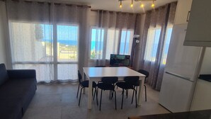 Een kamer met een eettafel, stoelen, een bank, een televisie en uitzicht op zee.