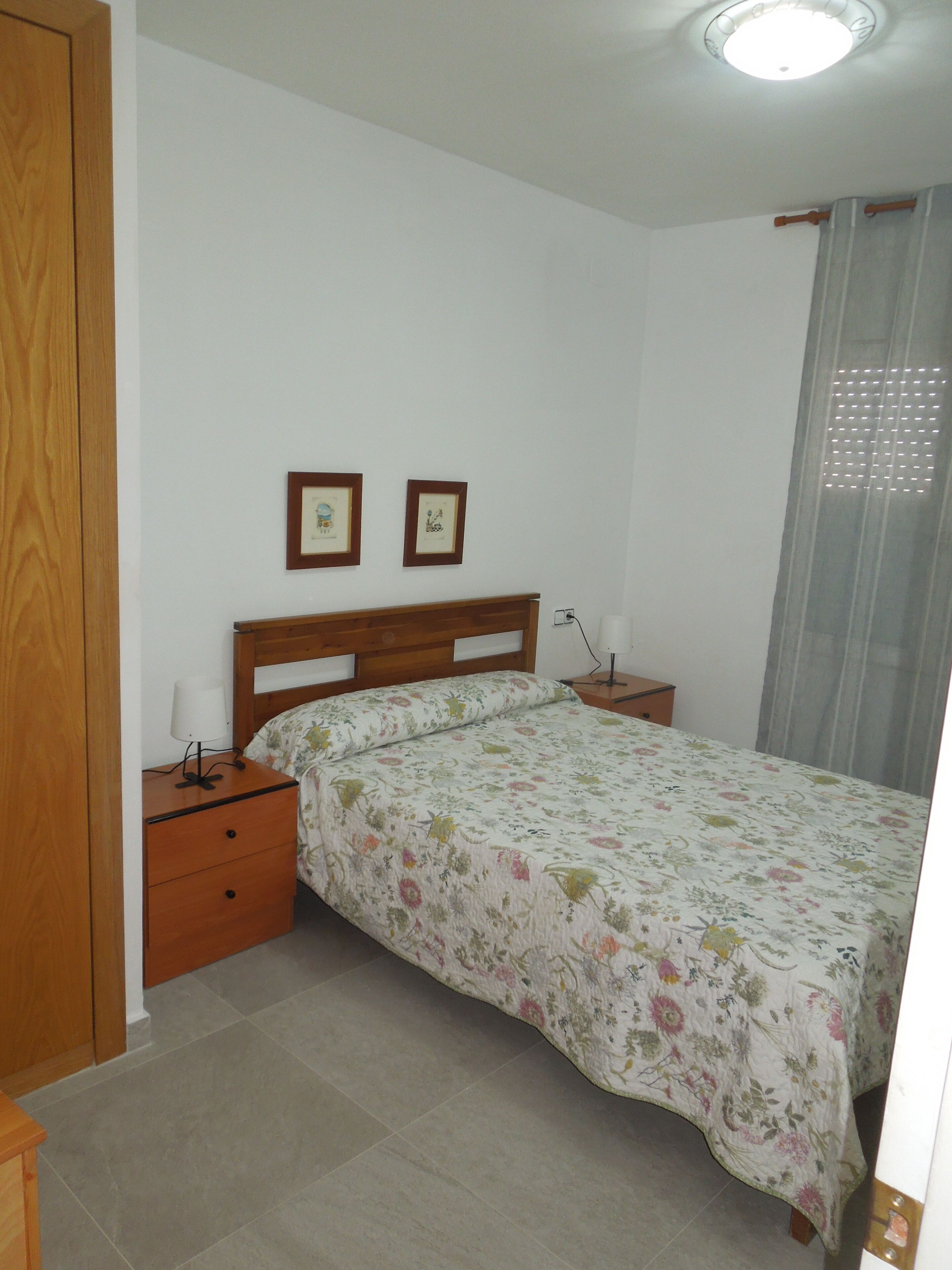 Um quarto com uma cama, mesas de cabeceira, um guarda-roupa de madeira e duas molduras na parede.