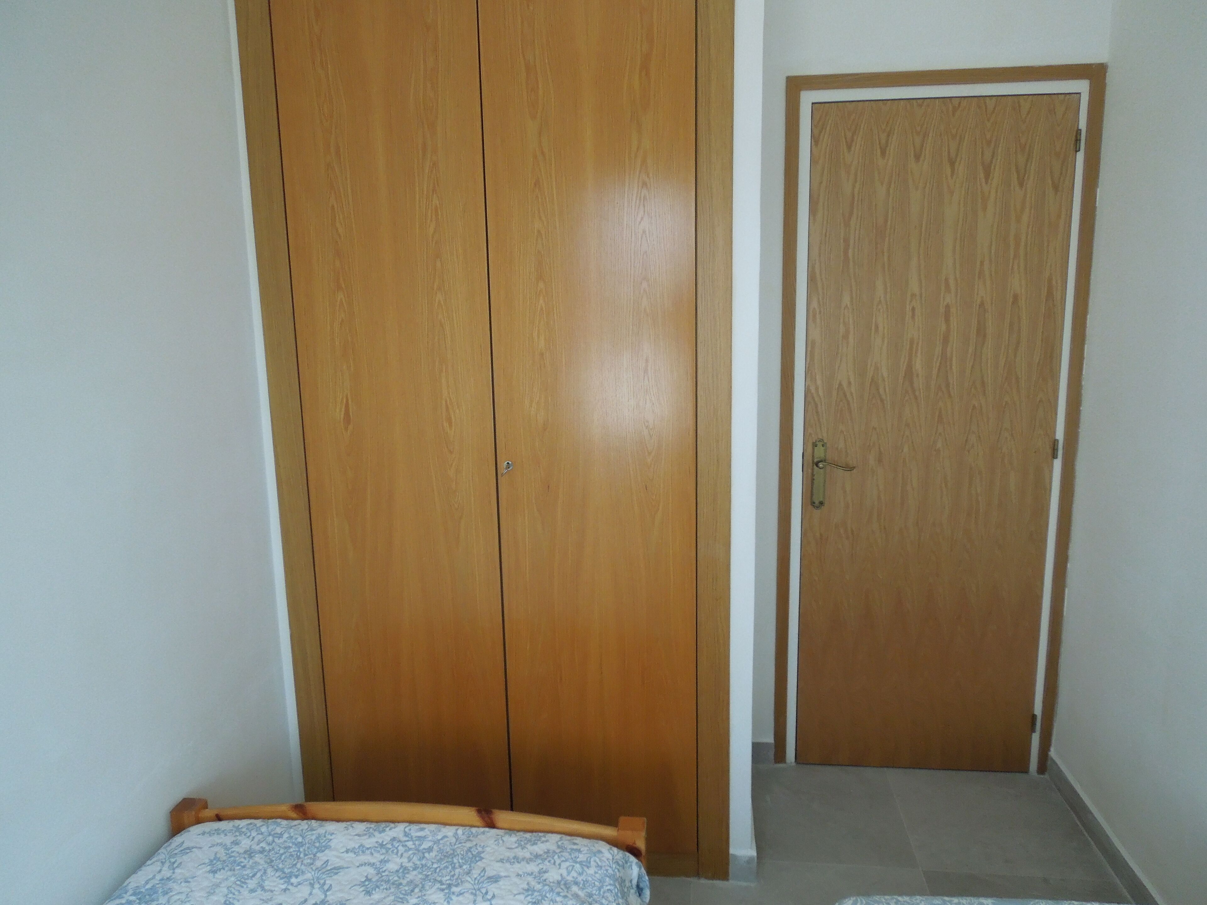 Une chambre avec une armoire en bois, une porte et un lit recouvert d’une couvre-lit à motifs.