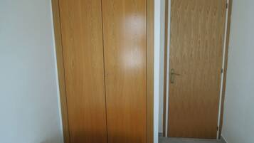 Une chambre avec une armoire en bois, une porte et un lit recouvert d’une couvre-lit à motifs.